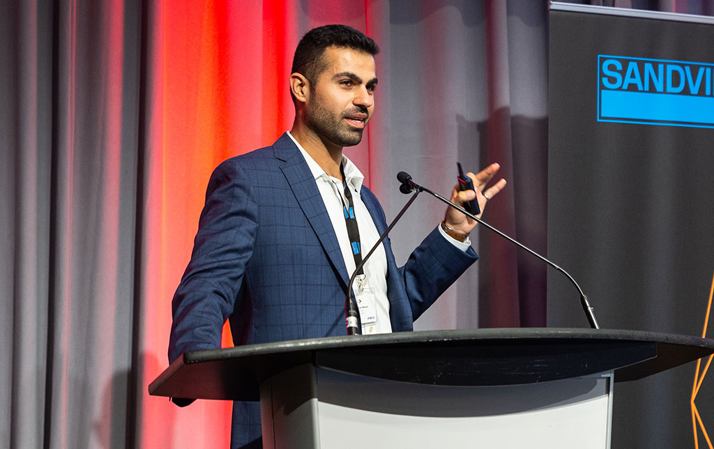Peyman Moeini presenting on stage at a lectern